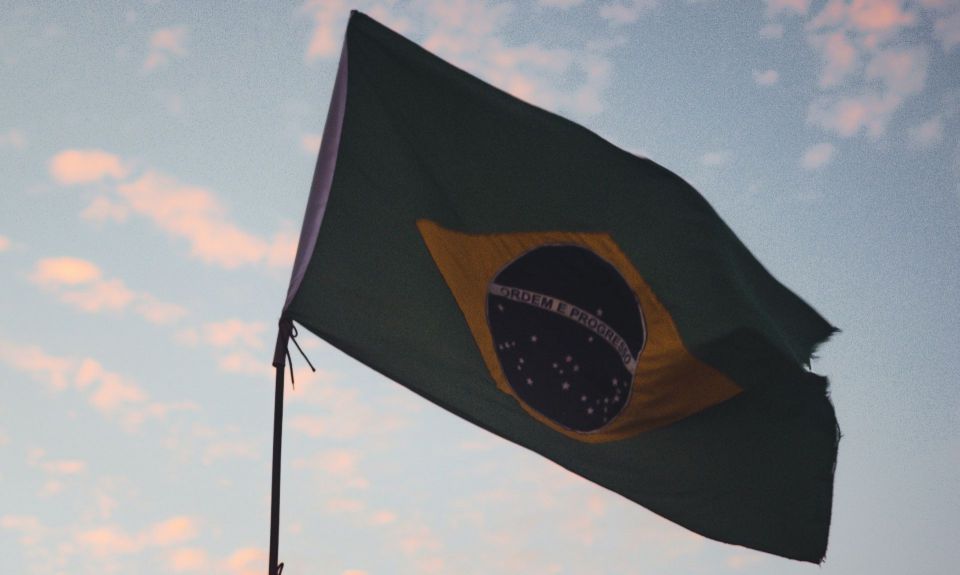 Brazilian flag against light blue sky filled with pink clouds