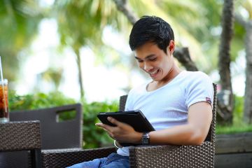 Man sitting outside, smiling at a tablet in his arms 